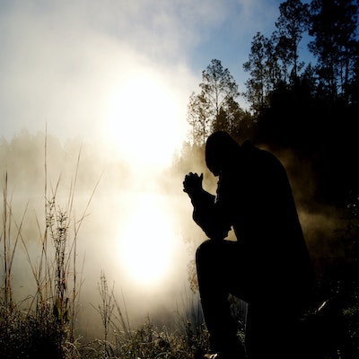 A person praying over a body of water during the day. 